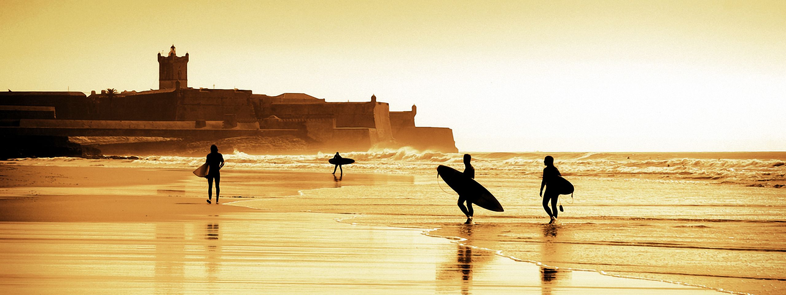 Surfers at sunset at Carcavelos Beach with the St. Julian de Barra fortress in the background